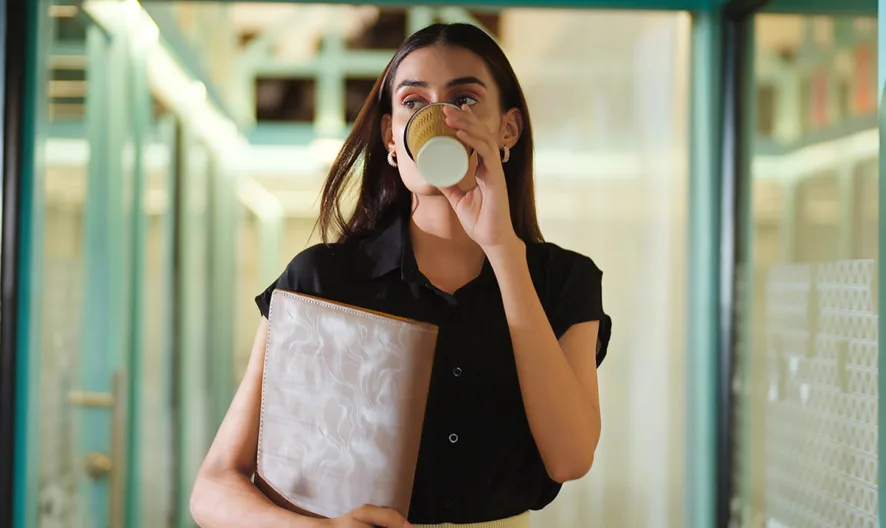 Woman drinking coffee while walking down a school hall