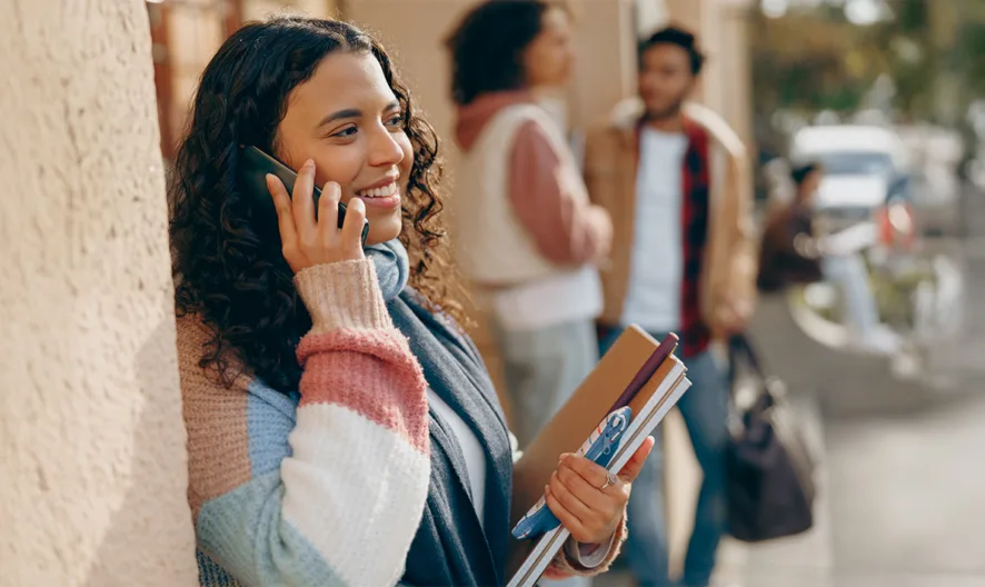 Image of a student talking on a cell phone while leaned against a wall.