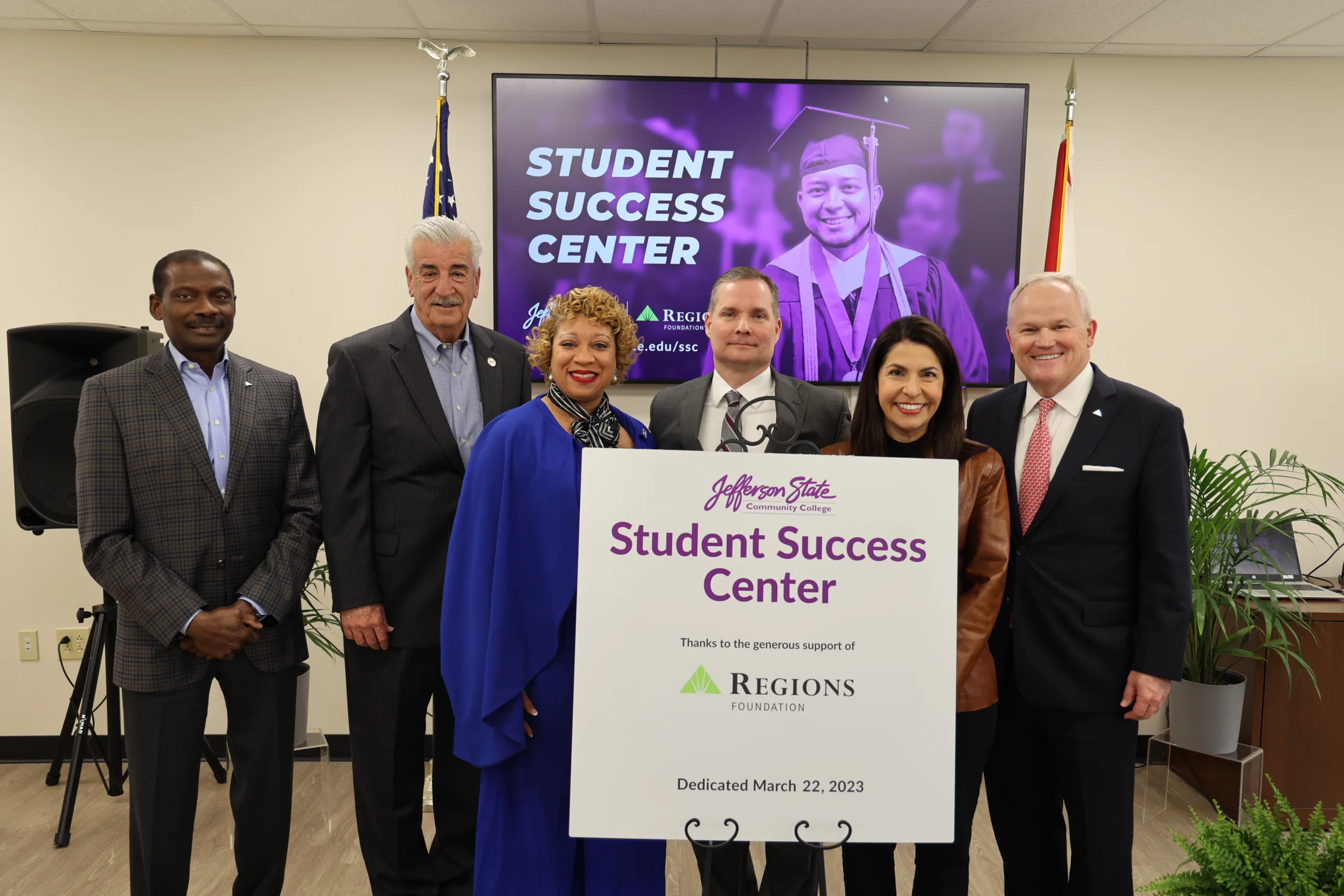 Six people stand smiling behind a sign reading Student Success Center with a large screen and flags in the background. The event appears to be a dedication ceremony on March 22, 2023, at Jefferson State Community College.