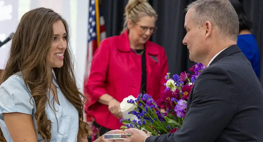 A man in a suit hands an award to a woman in a light blue blouse during a ceremony.