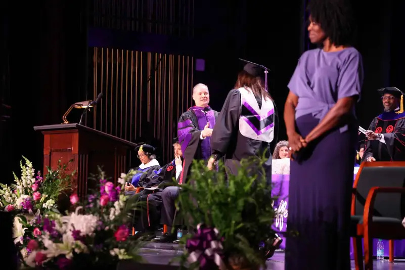 A graduate in cap and gown walks across a stage